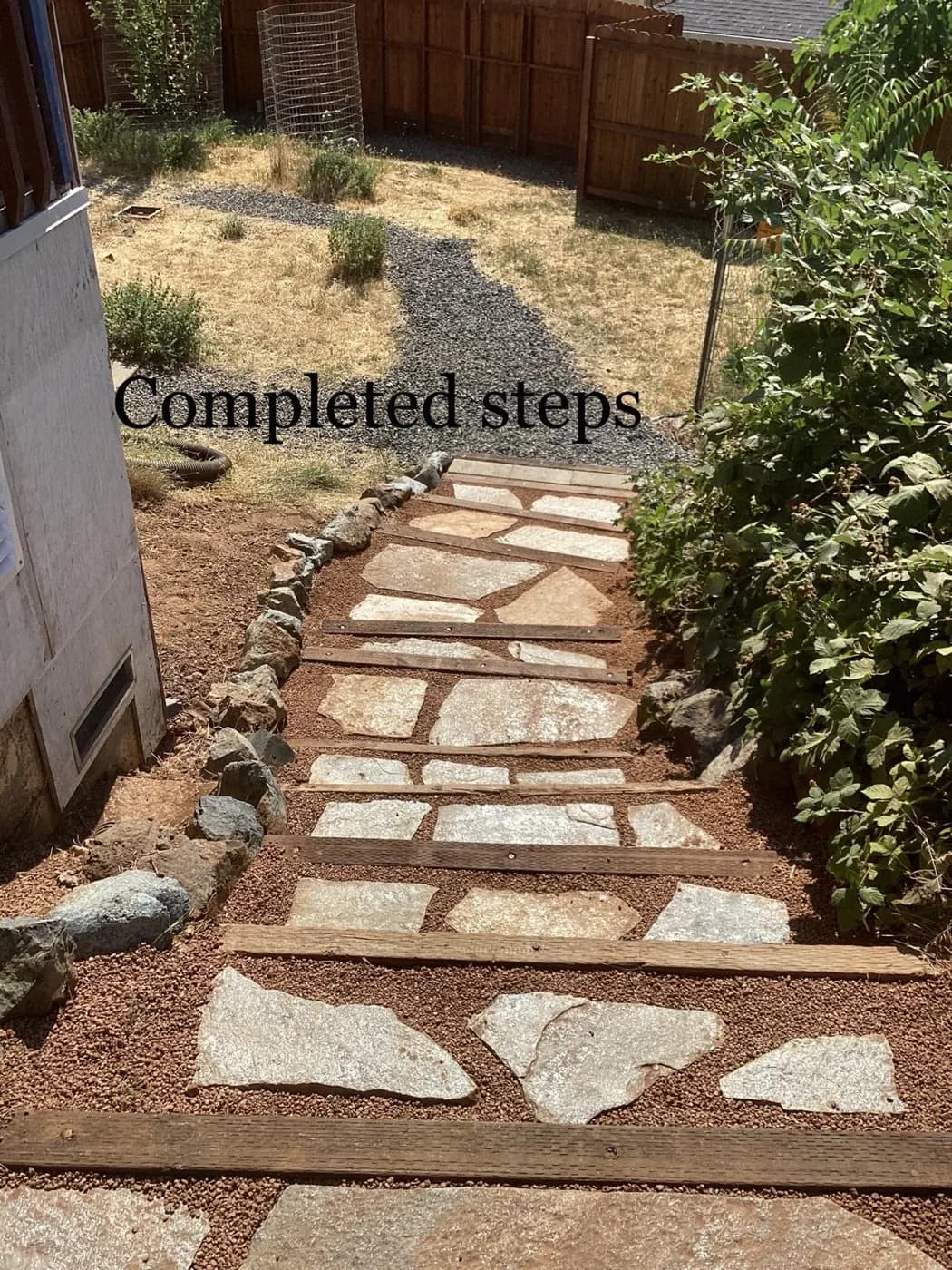 Flagstone steps set into a planted slope between a fence and a house wall