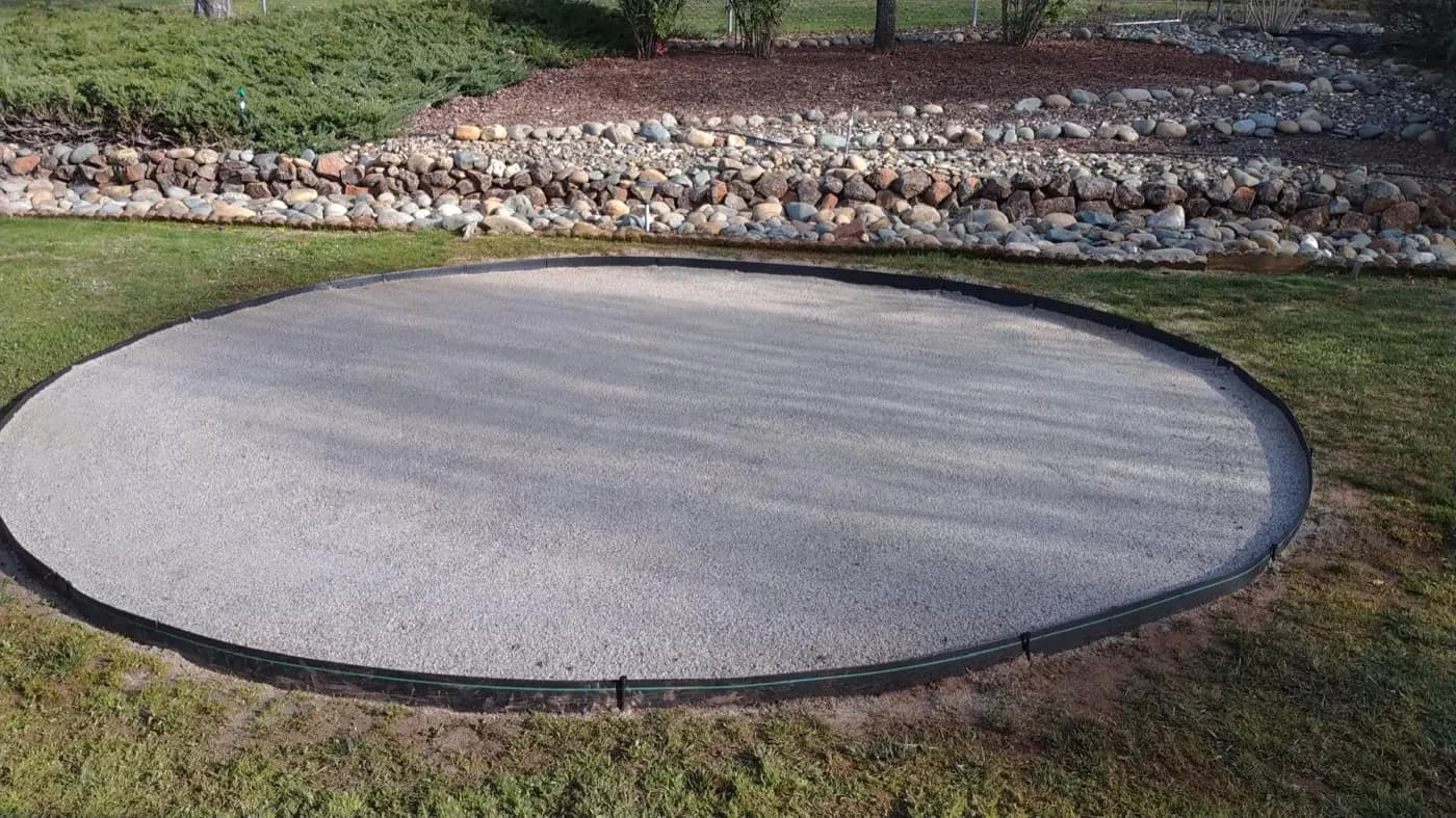 Finished circular gravel pad edged in steel with a river rock dry creek bed running past it