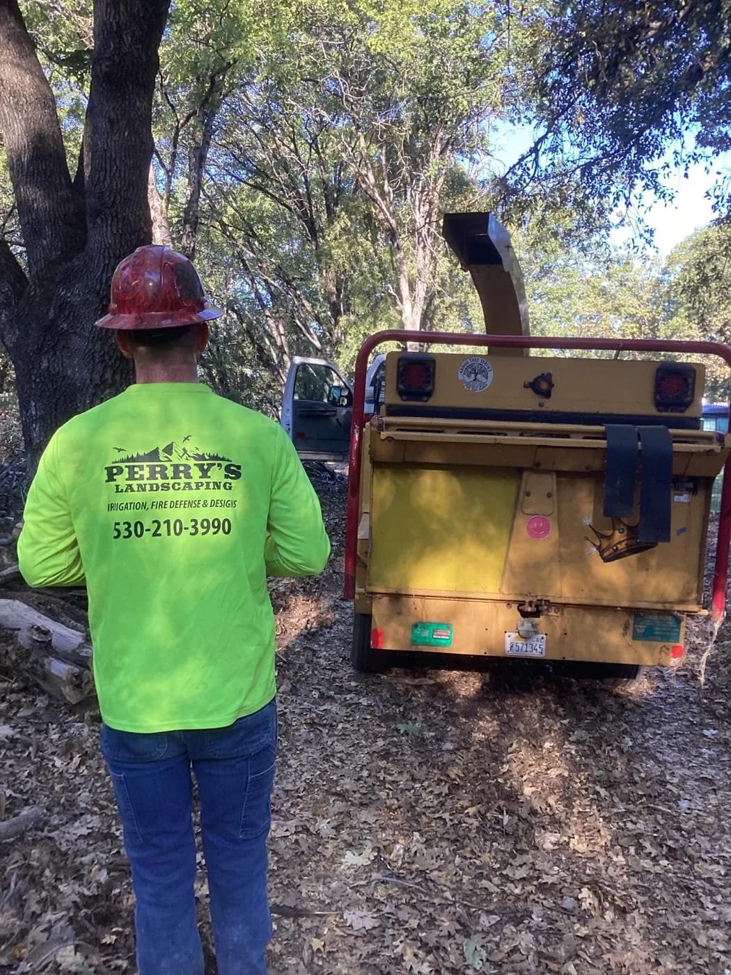 Perry's Landscaping crew member in a branded shirt beside the chipper on a job