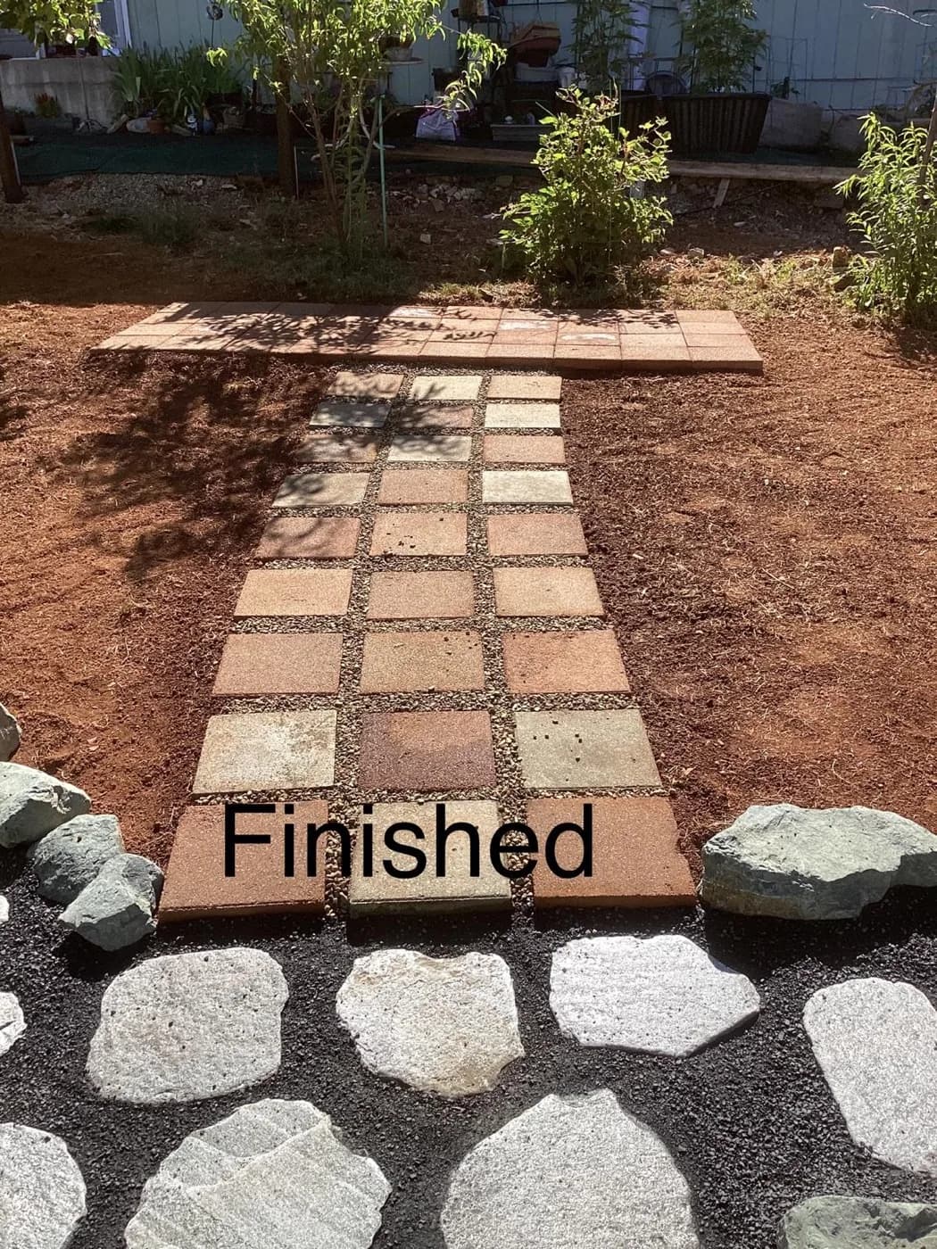 Square pavers and flagstone stepping stones set into fresh soil beside new plantings